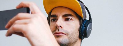 Man wearing black corded headphones while watching his phone