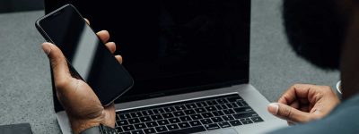 A man holding his cell phone sitting at a laptop computer