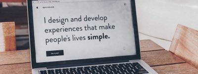 A laptop computer screen says “I design and develop experiences that make people’s lives simple.